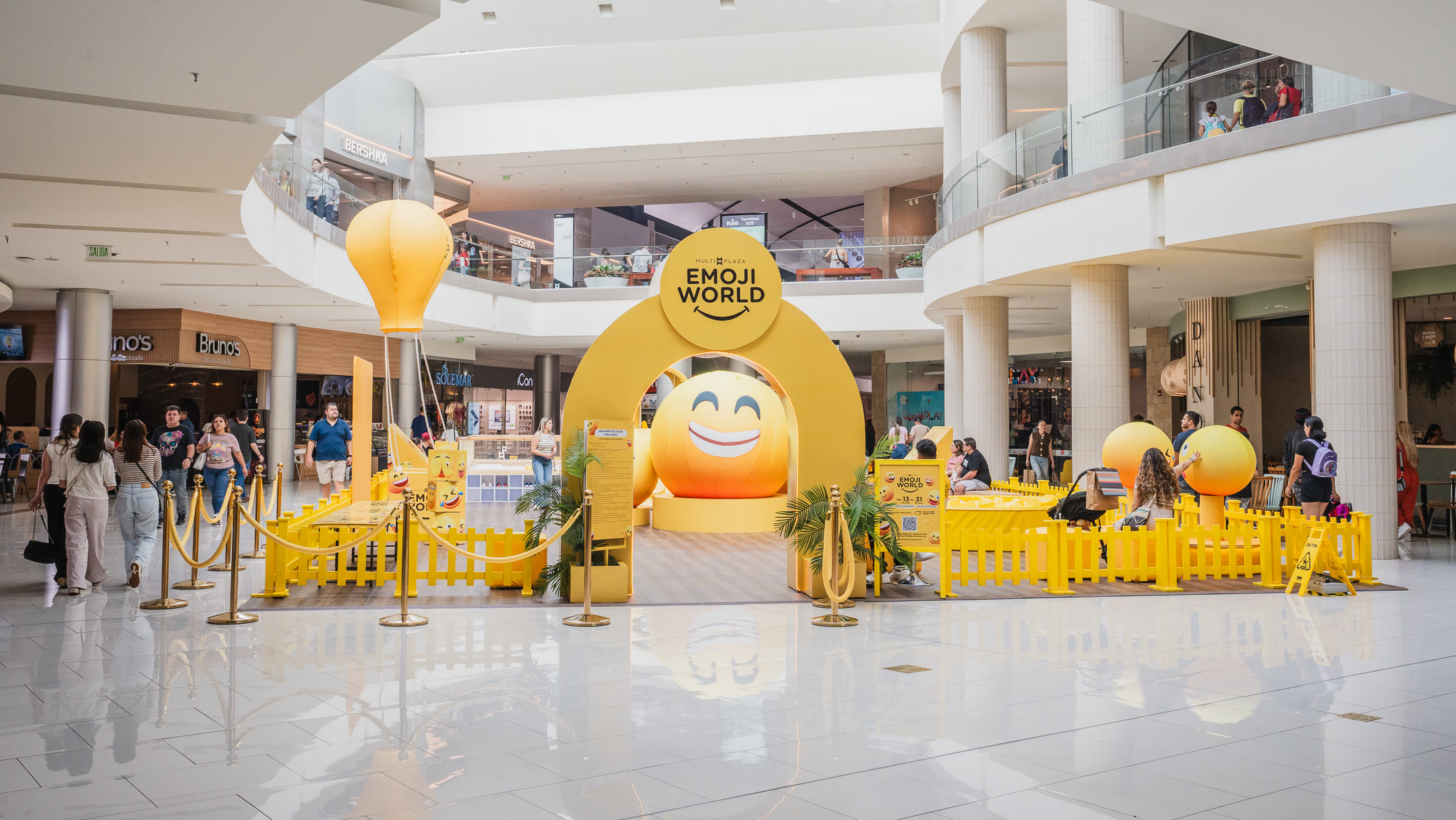 Vista frontal de Emoji World en Multiplaza, con gran arco amarillo, figuras emoji y zonas de juego para familias